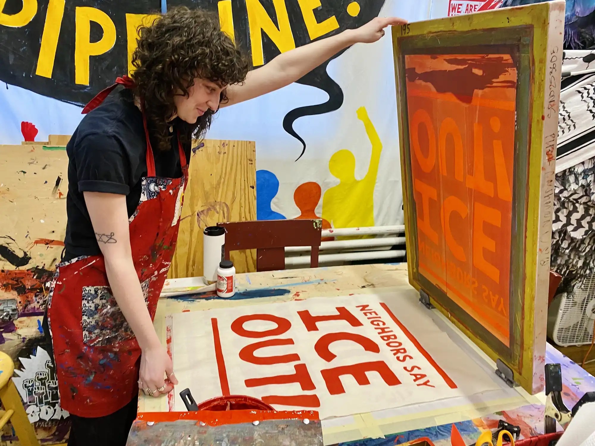 Artist stands at an open printing press after creating an "NEIGHBORS SAY ICE OUT" sign